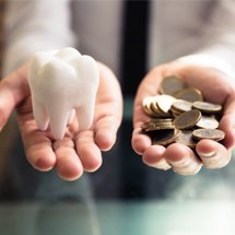 A person holding a model of a tooth and coins.