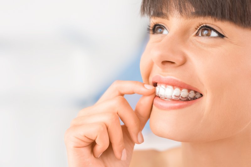 woman inserting Invisalign trays smiling